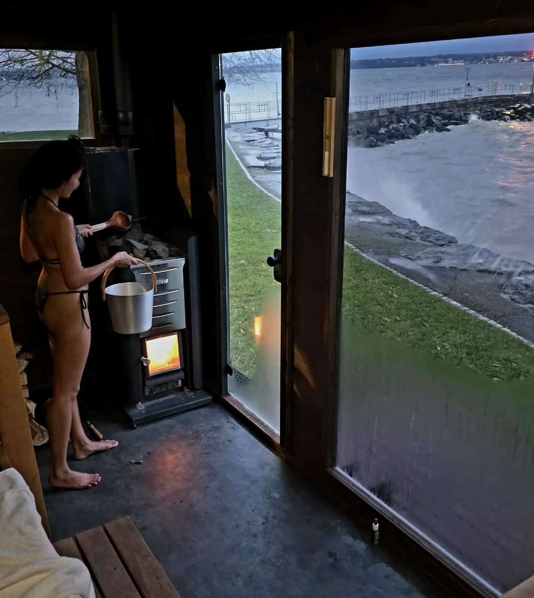 A customer in a swimsuit performs the traditional Löyly ritual by pouring water from a wooden ladle onto hot stones in a wood-burning sauna at Plage du Débarcadère in Anières on Canton of Geneva.